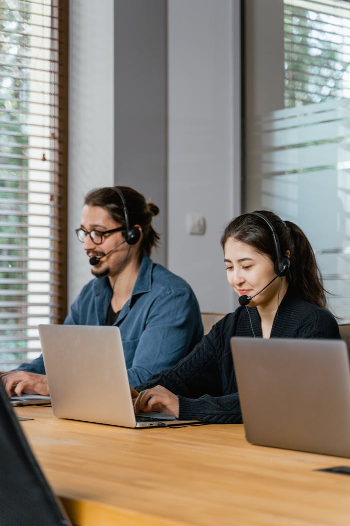 Two call center agents working diligently with laptops and headsets in a modern office setting.